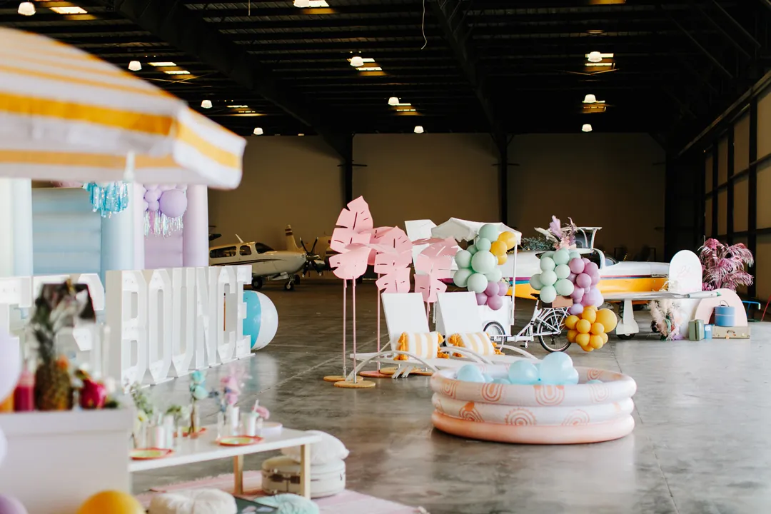 Wide view of the summer styled shoot at The Executive Hangar with an inflatable pool, lounge chairs, popsicle cart and plane