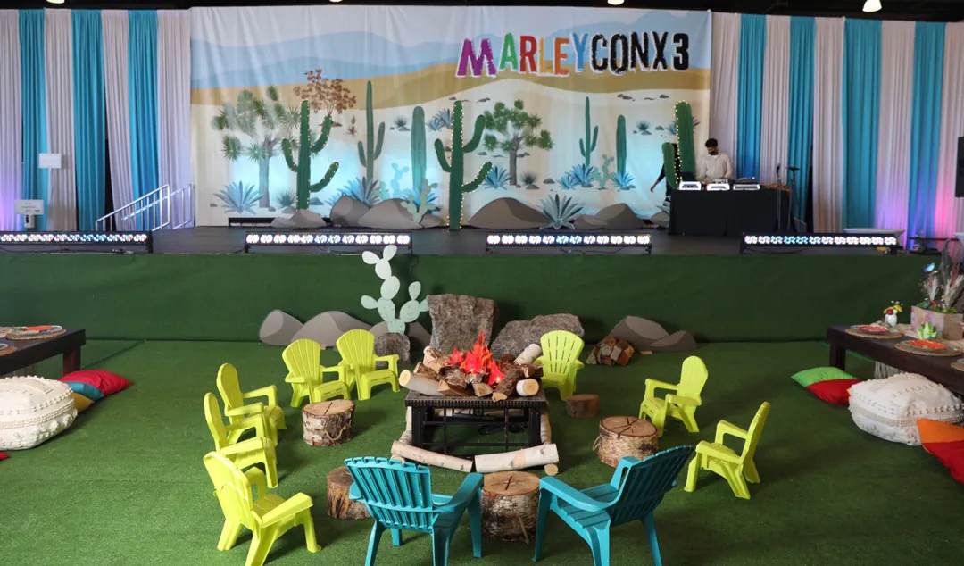 MarleyCon x 3 desert stage with cactus backdrop, DJ, faux campfire and lime green kids chairs inside The Executive Hangar