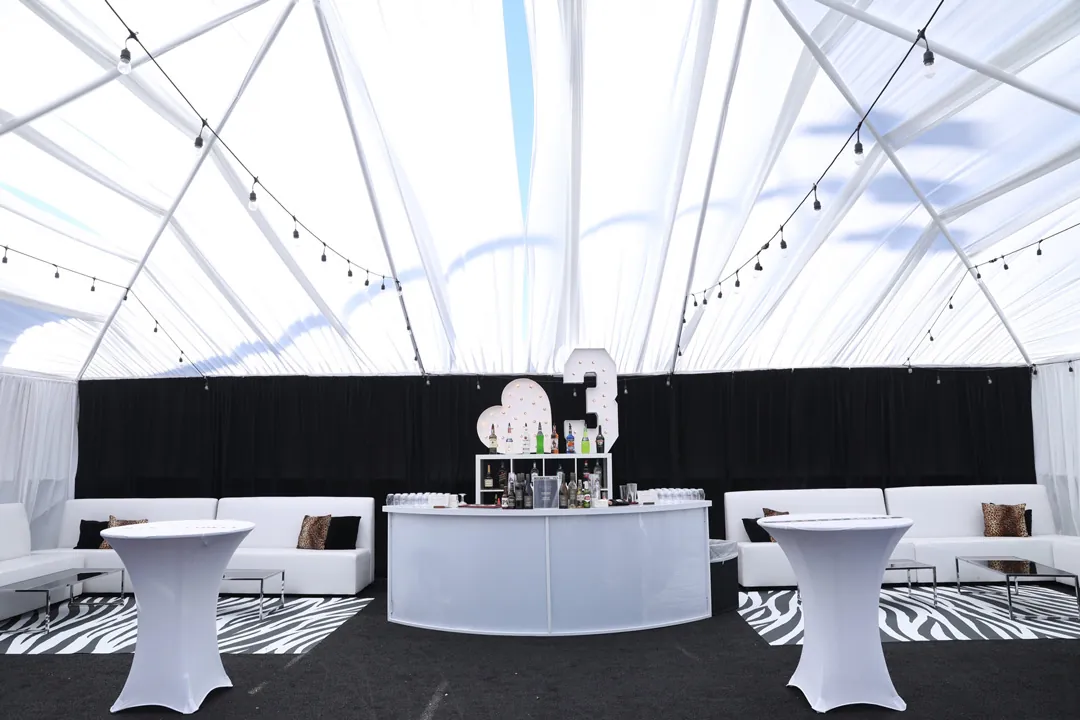 Clear-top adult lounge tent with white bar, marquee number 3, zebra rugs and white sofas at The Executive Hangar