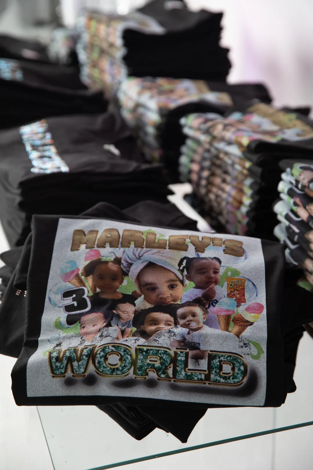 Stacks of black MarleyCon merch t-shirts printed with a Marley's World baby photo collage