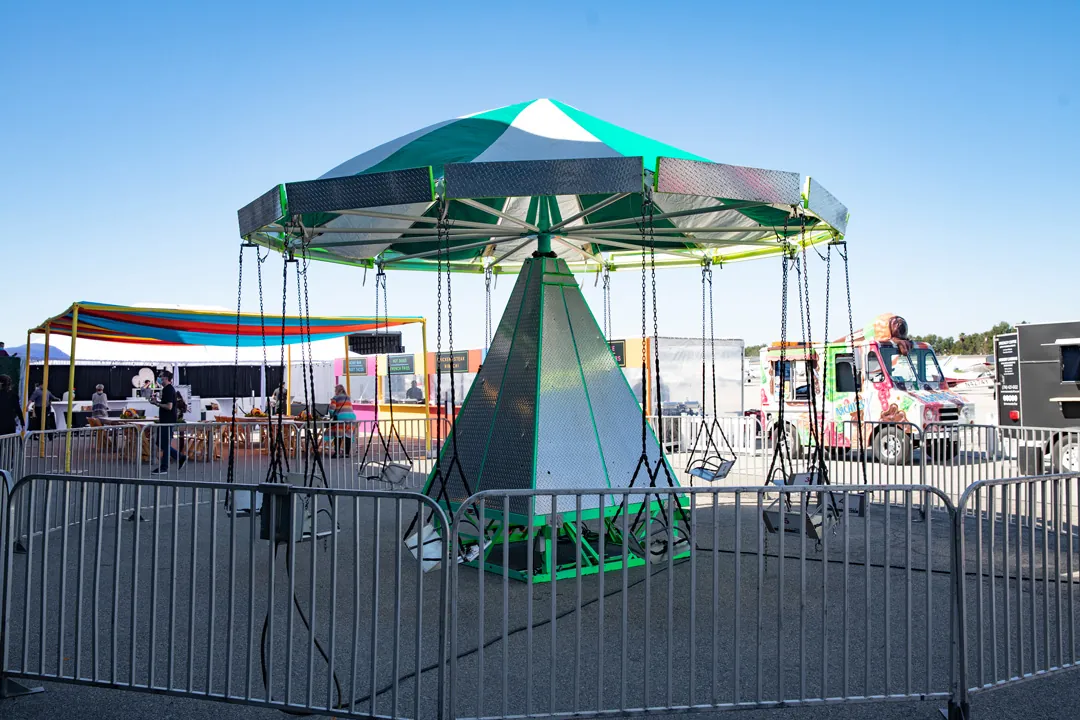 Green and white carnival swing ride on the tarmac at The Executive Hangar with food stations and trucks behind