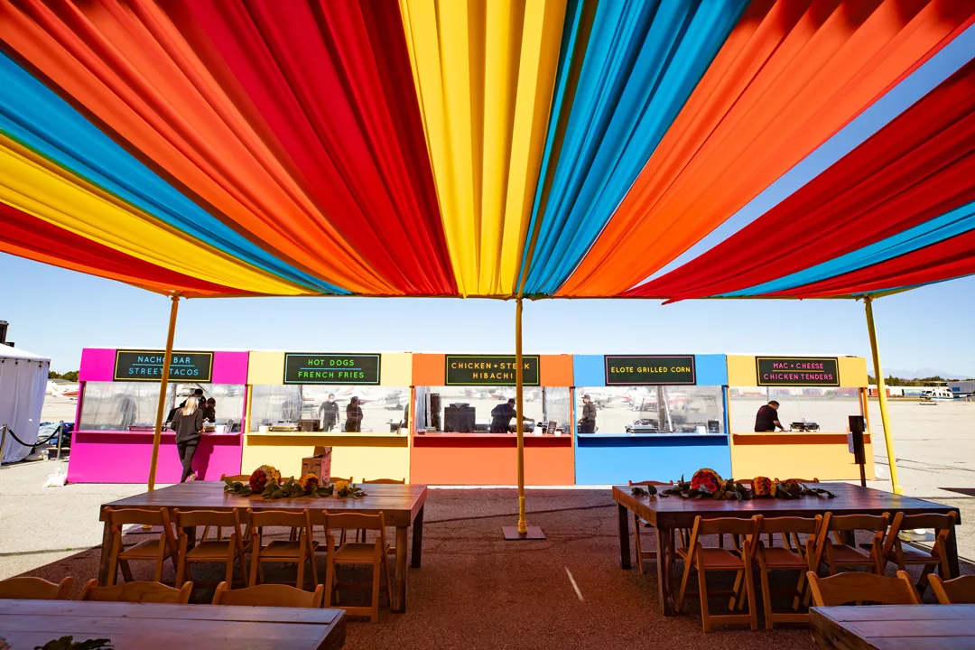 Colorful striped canopy over Jay's Catering food stations for nachos, tacos, hibachi, elote and mac and cheese on the tarmac