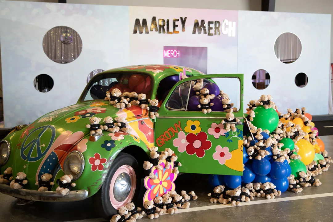 Green flower-power VW Beetle covered in teddy bears and balloons at the Marley Merch booth inside The Executive Hangar
