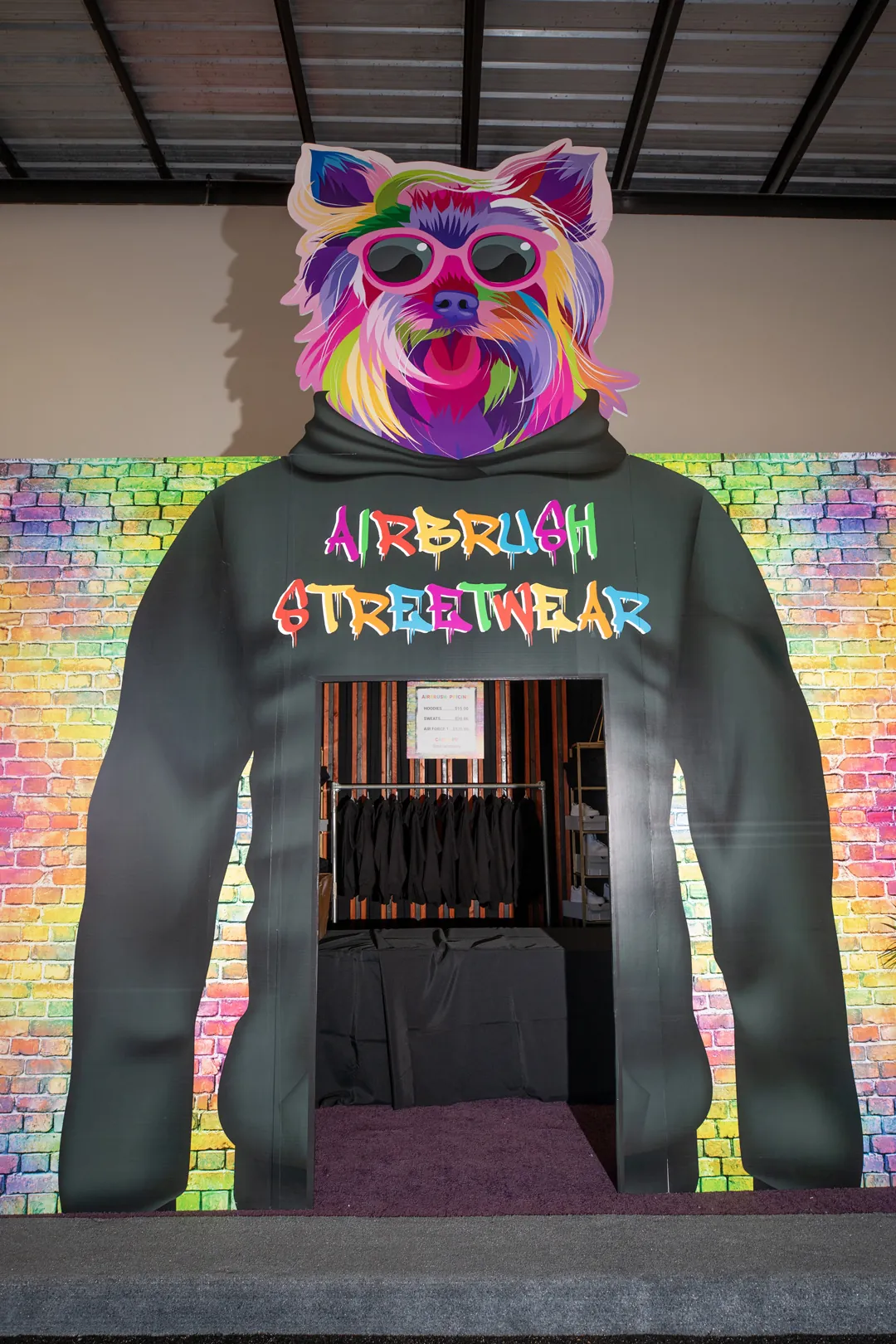Airbrush Streetwear booth shaped like a giant hoodie with a rainbow dog graphic on a colorful brick backdrop
