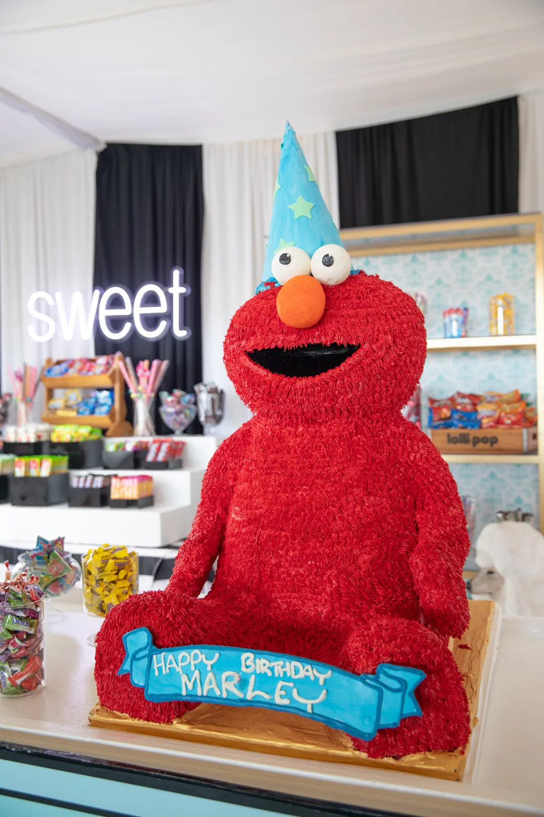 Larger than life red Elmo birthday cake in a party hat with a Happy Birthday Marley banner at the sweet shop
