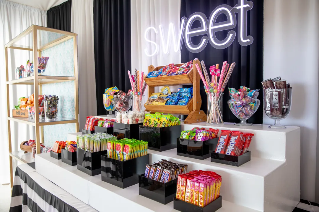 Sweet shop candy display with neon sweet sign, lollipops, Twizzlers and Skittles on white tiered shelves