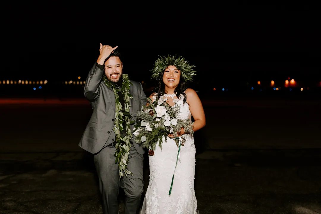 James throws a shaka and Roni laughs in her greenery crown on the tarmac after their night helicopter flight