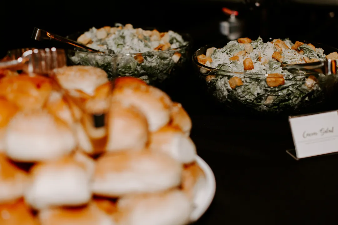 Buffet with stacked dinner rolls and bowls of Caesar salad topped with croutons at the hangar reception