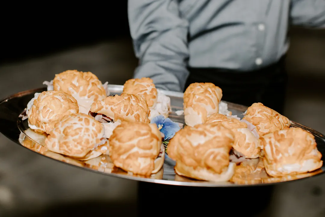 Tray-passed mini sandwiches on toasted buns held by a Jay's Catering server at The Executive Hangar