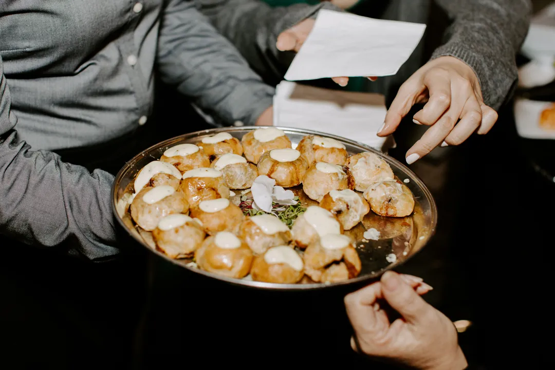 Server offers a tray of savory bites topped with cream sauce and edible flowers at cocktail hour