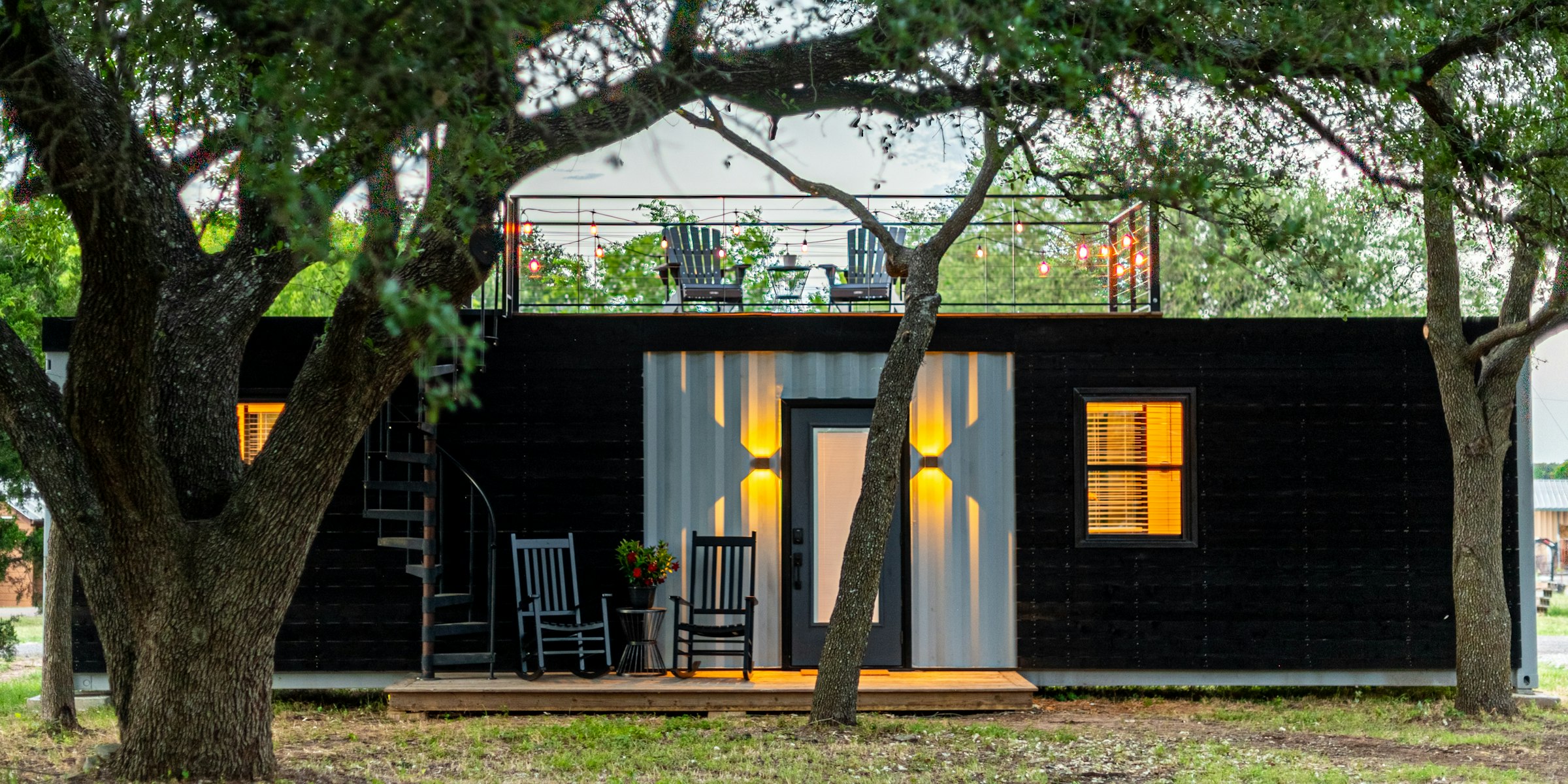 Backyard ADU cottage with lit windows under oak trees
