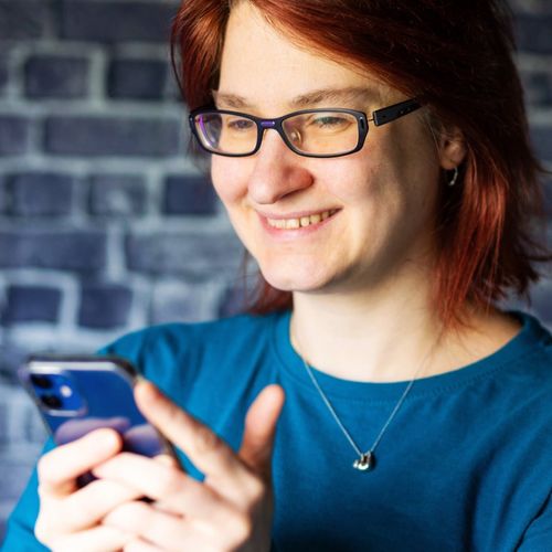 Judith, Textmentorin und Texterin von federPott, schreibt lächelnd eine Textnachricht auf ihrem Smartphone