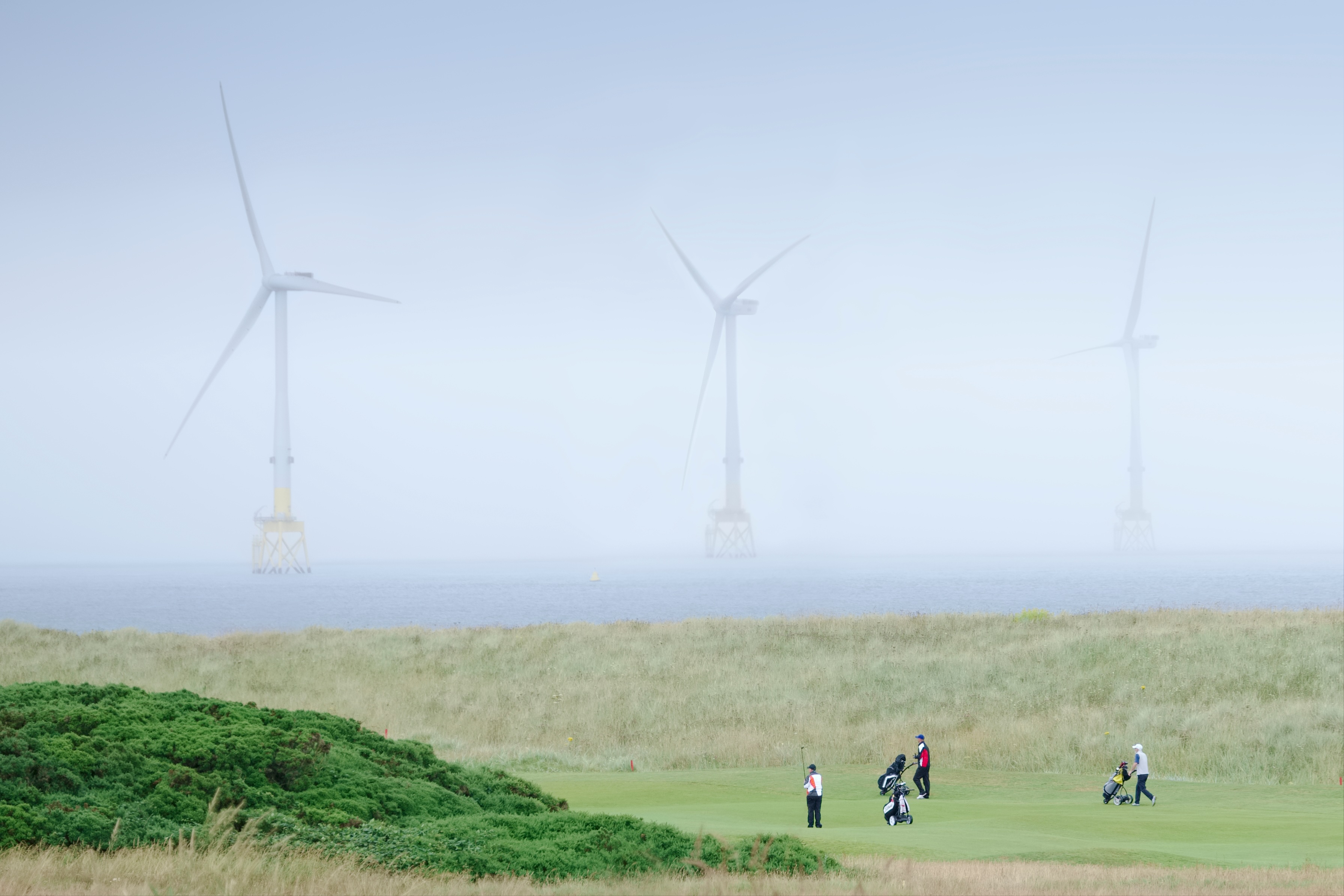 Balmedie, Aberdeen / Scotland, UK - 7th August 2019: Donald Trump golf course showing wind farm turbines and golfers in the North Sea