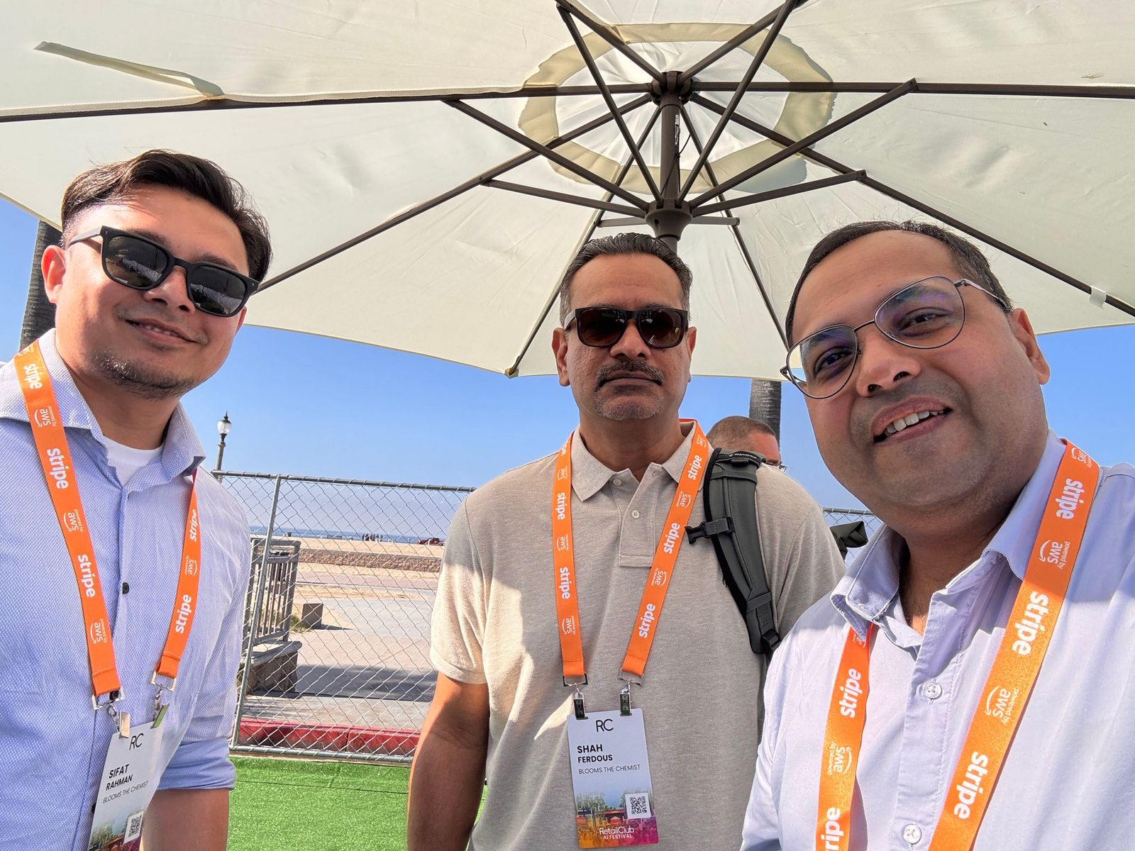Abhijeet Mishra con dos asistentes bajo una sombrilla, con la playa y el océano al fondo