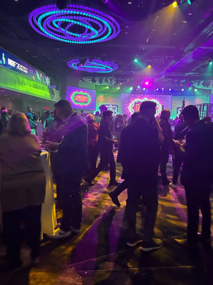 A crowded evening reception under purple and teal lighting with NRF screens
