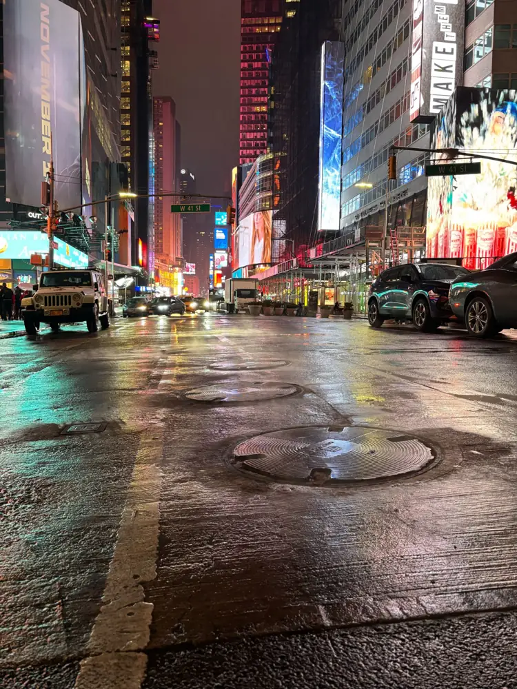 A wet Times Square street at night reflecting billboard lights near West 41st Street