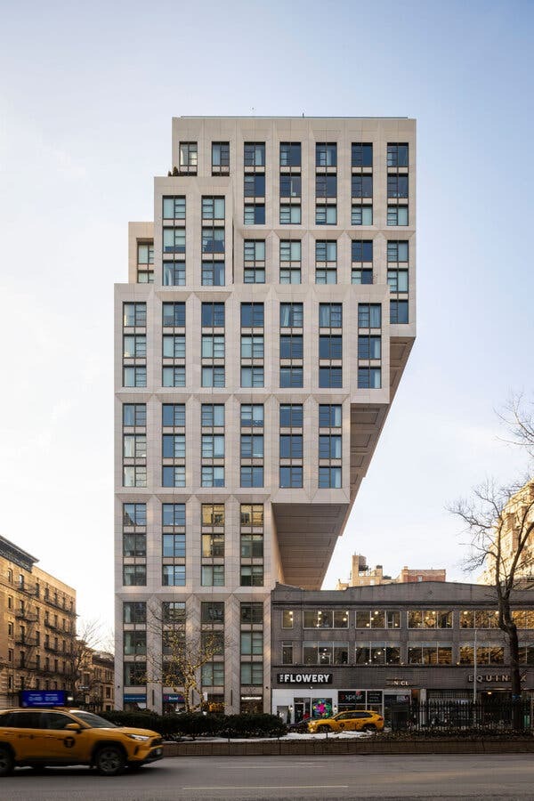 A street-level view of a condominium building that goes up and then over a smaller building.