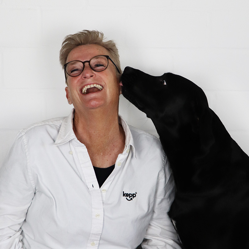 Porträt von Inga Kepp mit einem schwarzen Labrador, der ihr ein Küsschen gibt