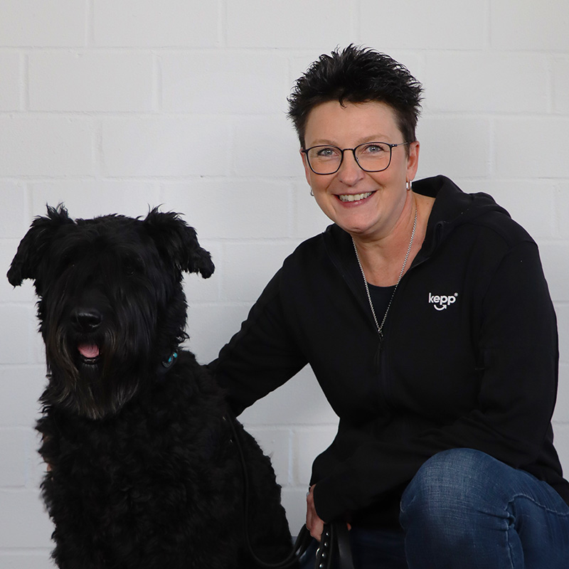 Porträt von Nicole Kellner mit einem schwarzen Hund an ihrer Seite
