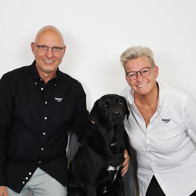 Porträt von Michael Kepp und Inga Kepp mit ihrem schwarzen Labrador Knut, der zwischen den beiden sitzt