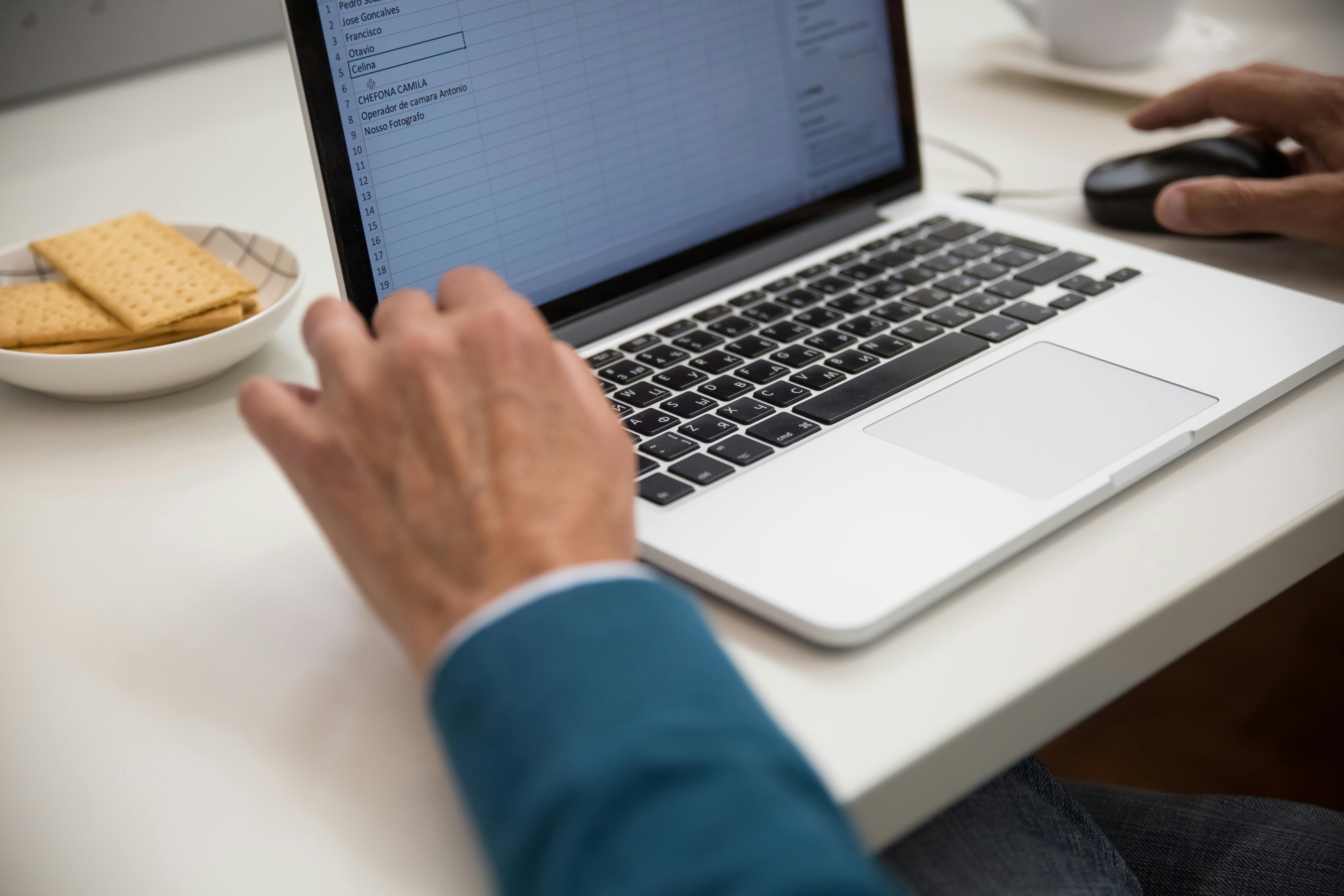 Person working on a laptop with a spreadsheet open, with a plate of crackers on the desk nearby.