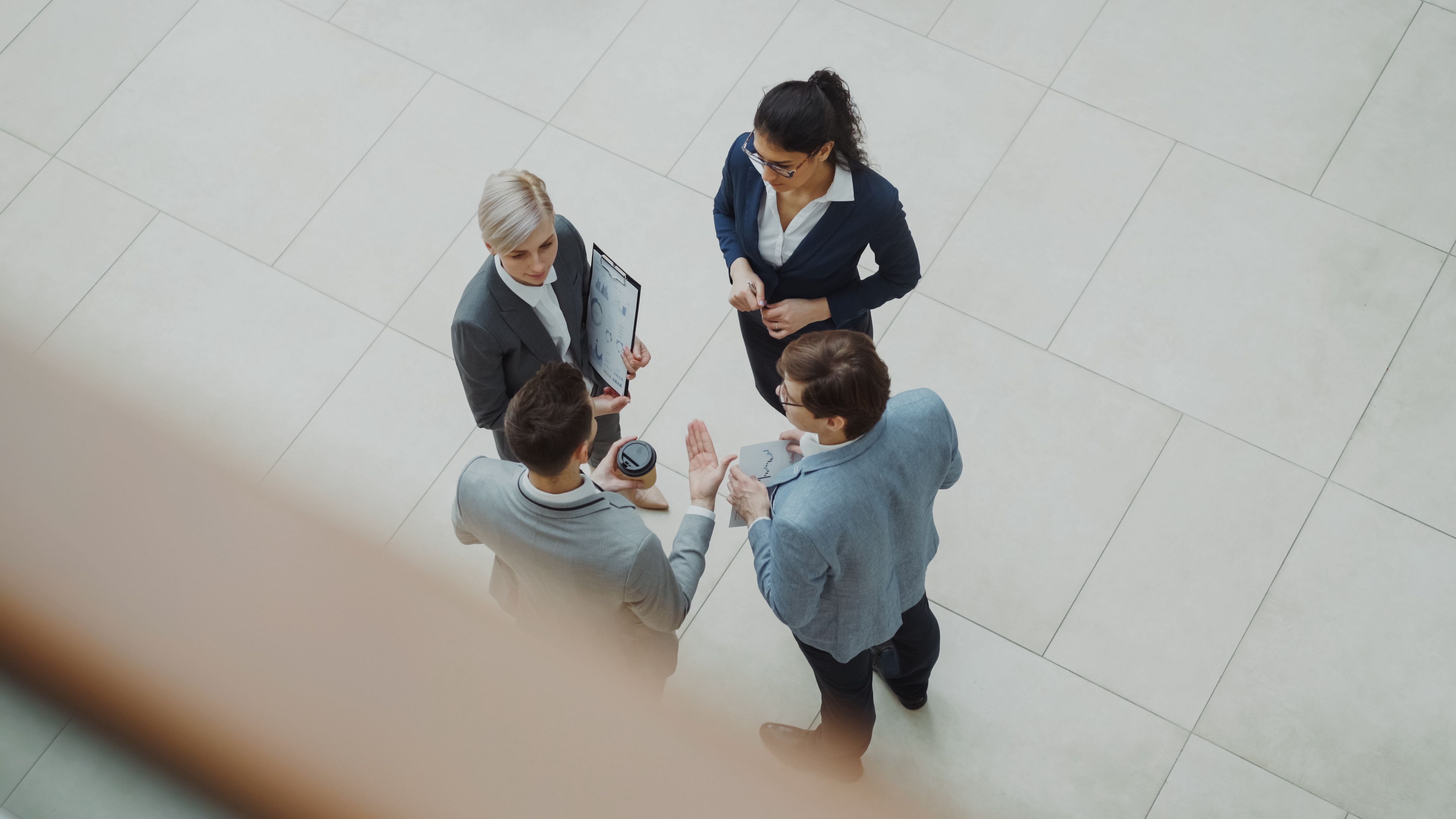 Overhead view of four coworkers standing in a circle discussing charts and reports in an office lobby.