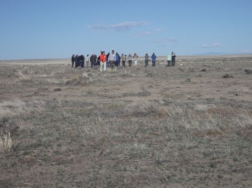 A diverse group of people grouped together in the plains surrounded by scrub grass and clear skies.