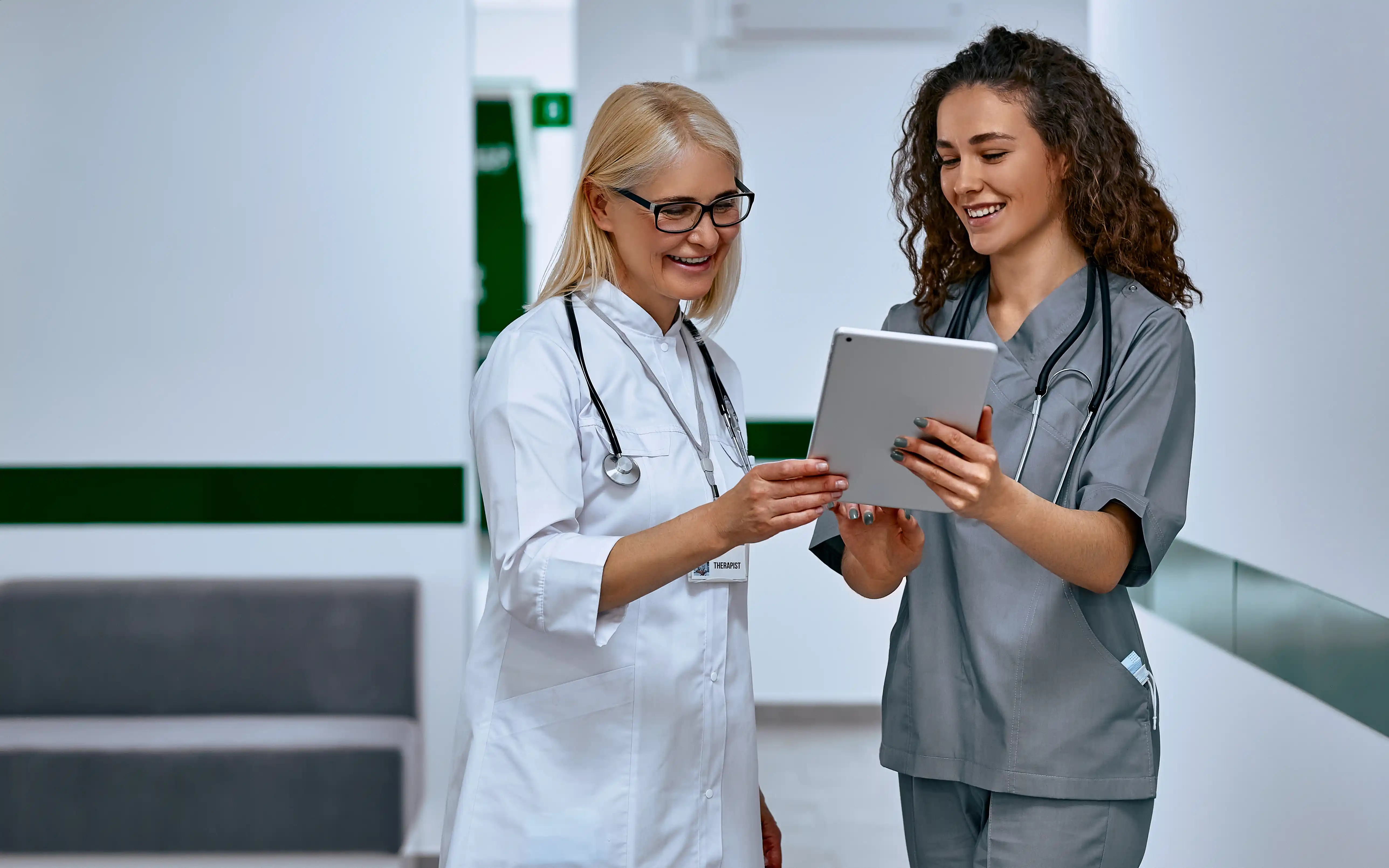 Therapist and nurse discuss workflow optimization while referring to platform on tablet