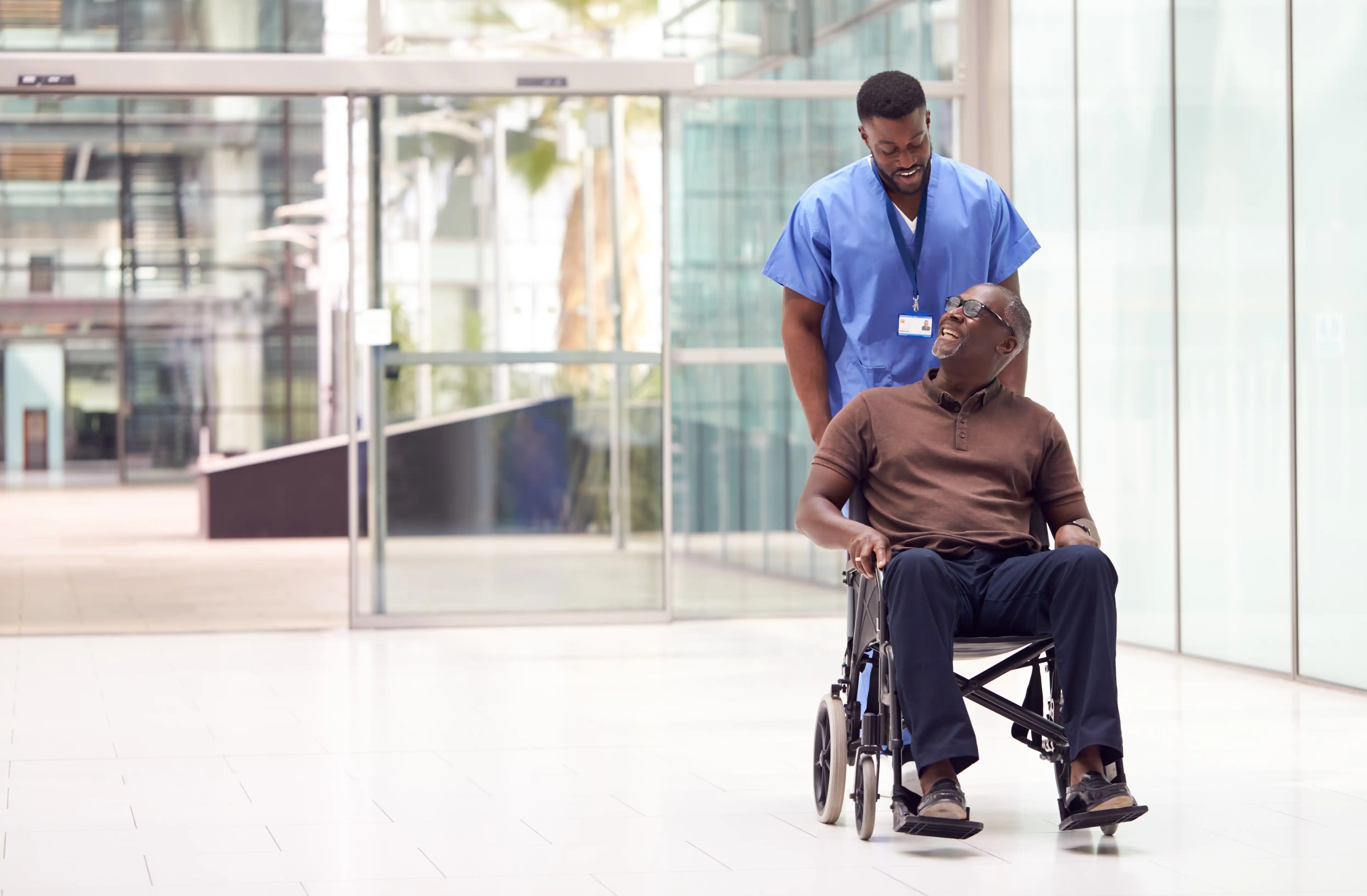 Patient in wheelchair pushed by hospital attendant through lobby.