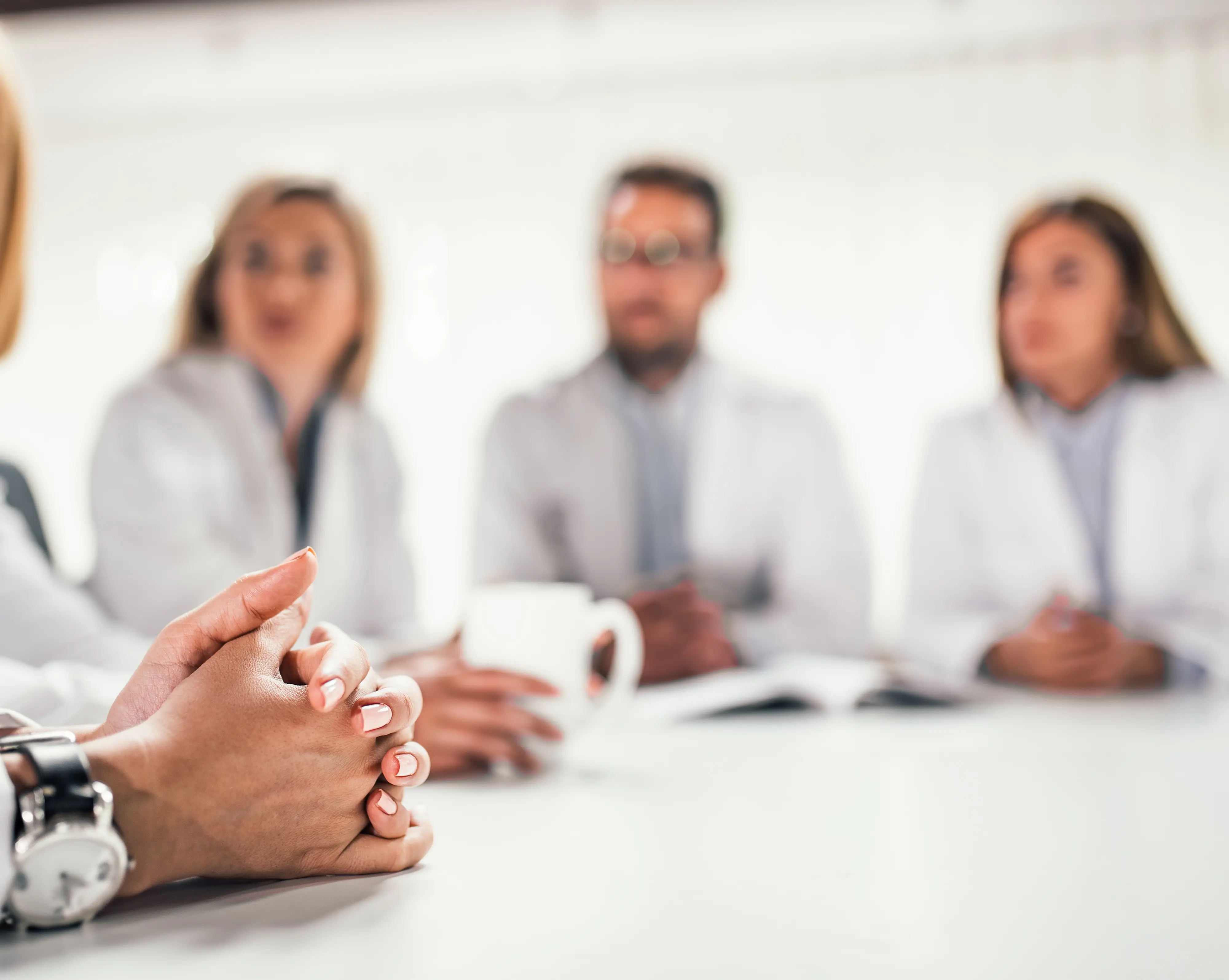 Medical workers in a meeting discussing PROMs, close up on clinician hands with other clinicians in background.