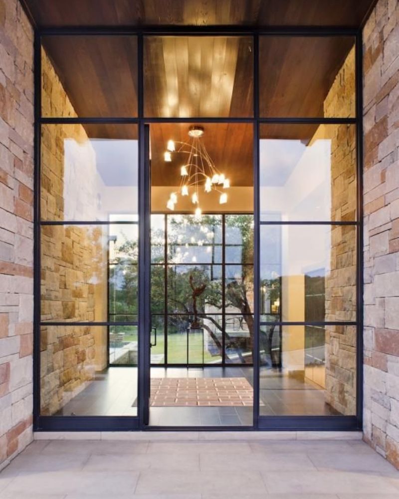 Eingangstür im Industrial Look aus schwarzem Stahl und Glas mit Natursteinfassade.
