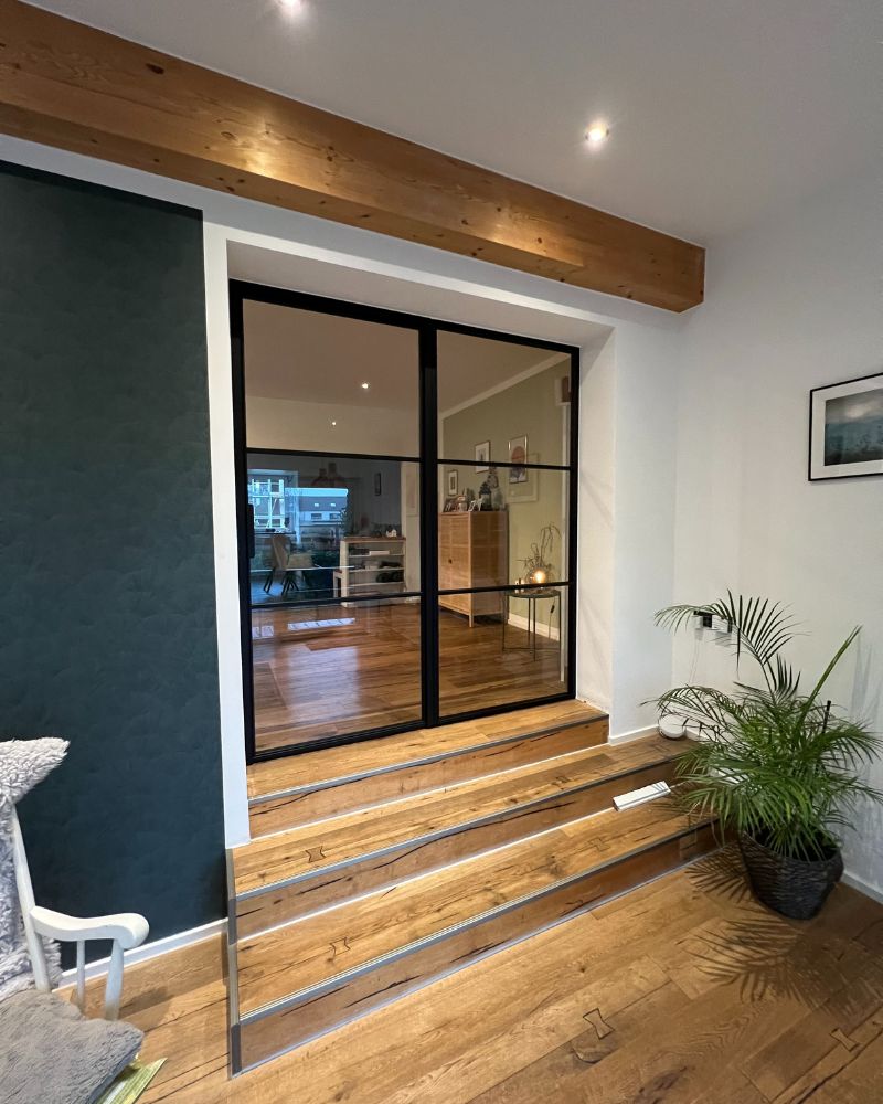 Innentür im Industrial Design aus schwarzem Stahl und Glas, eingebaut über einer Holztreppe mit gemütlichem Wohnambiente.