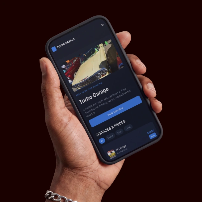 Hand holding smartphone displaying Turbo Garage website with car image, services, and prices.