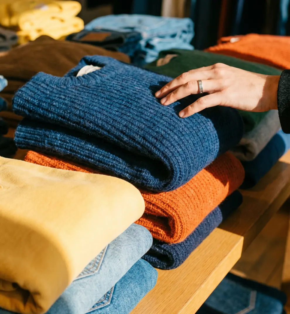 Customer hand touching folded sweaters on boutique display table