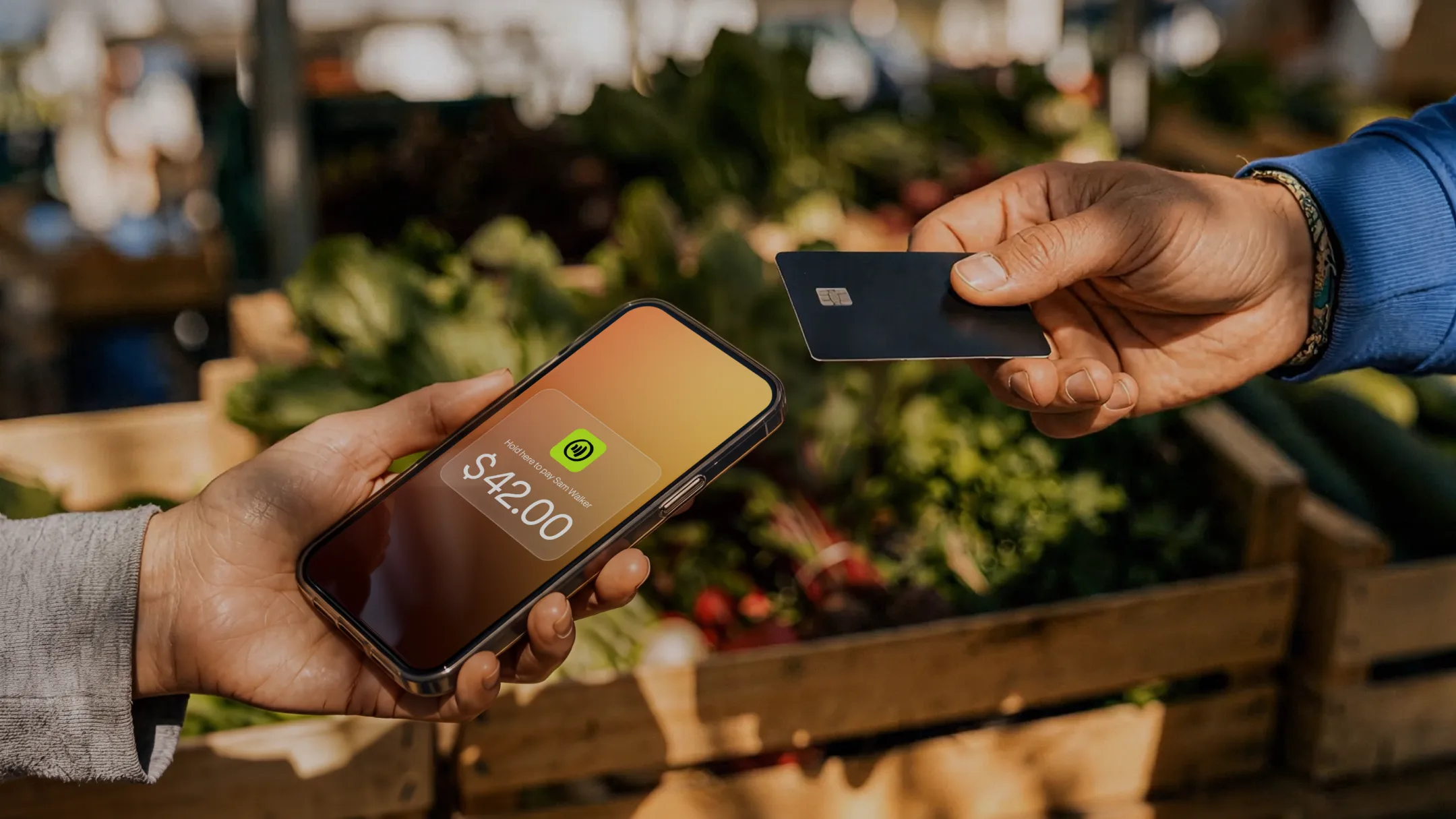 Merchant accepting a card tap on a phone for $42.00 at a farmers market