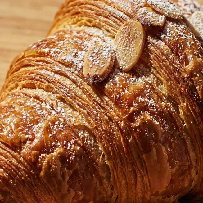 Close-up of a golden-brown almond croissant topped with sliced almonds and powdered sugar.