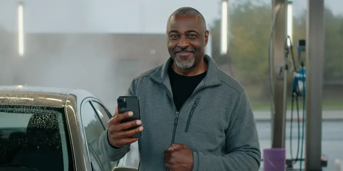 best credit card processing for small business man smiling while holding smartphone beside a car at a car wash station