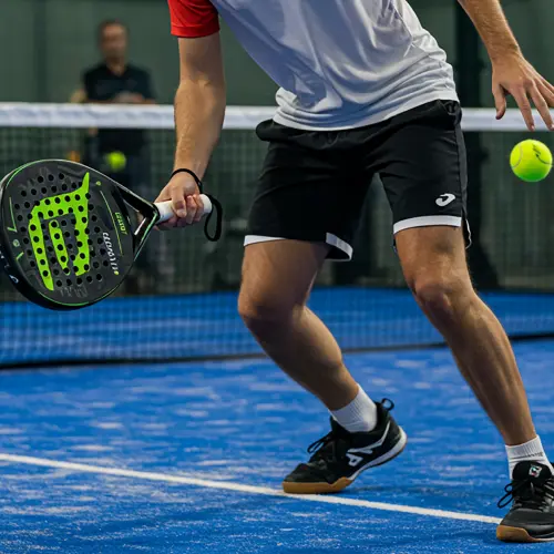 Close-up of a padel player in action, positioning to hit a ball during a competitive match on a blue indoor court.