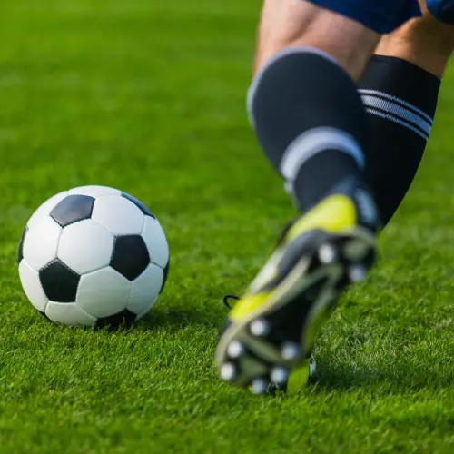 Close-up of a soccer player approaching a football on a grass field, moments before striking the ball during play.