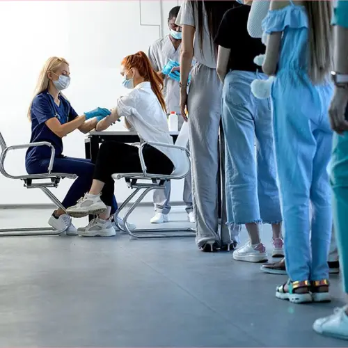 Patients waiting in line at a healthcare facility while medical staff provide care.