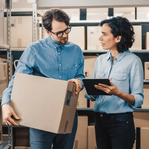 Warehouse staff managing inventory and logistics operations using a package and tablet.