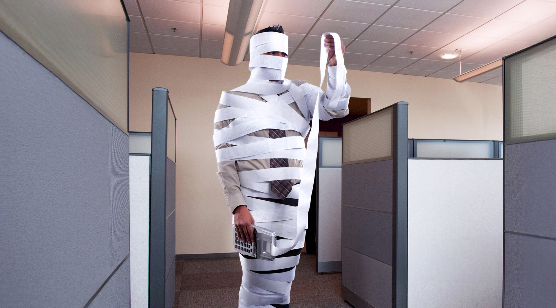 Un homme recouvert d'une bande infinie de reçu papier qui regarde sa calculette