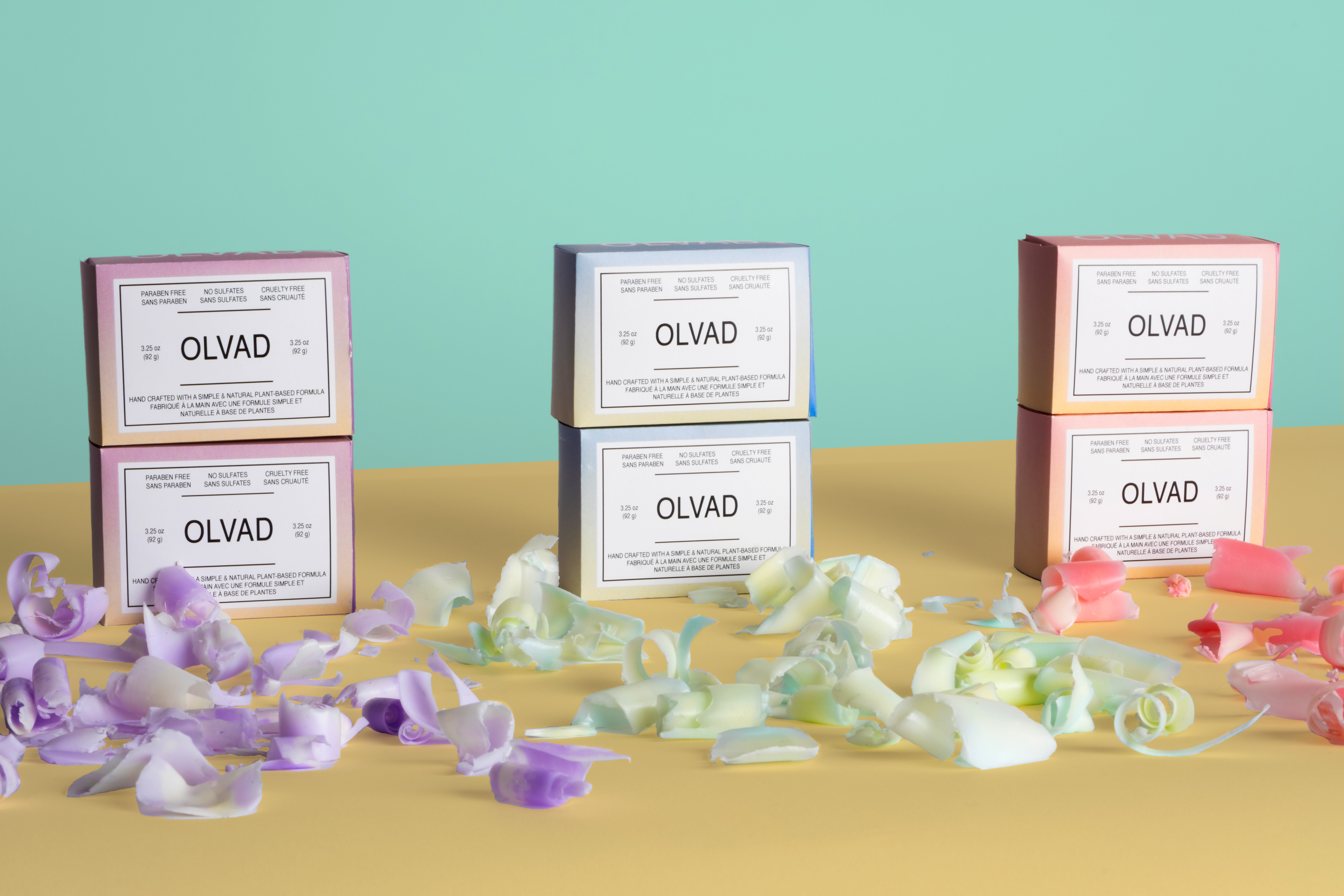 A product photo consisting of 3 package design variations in a single line. The 3 variations has one package stacked on top on a clean yellow tan background 