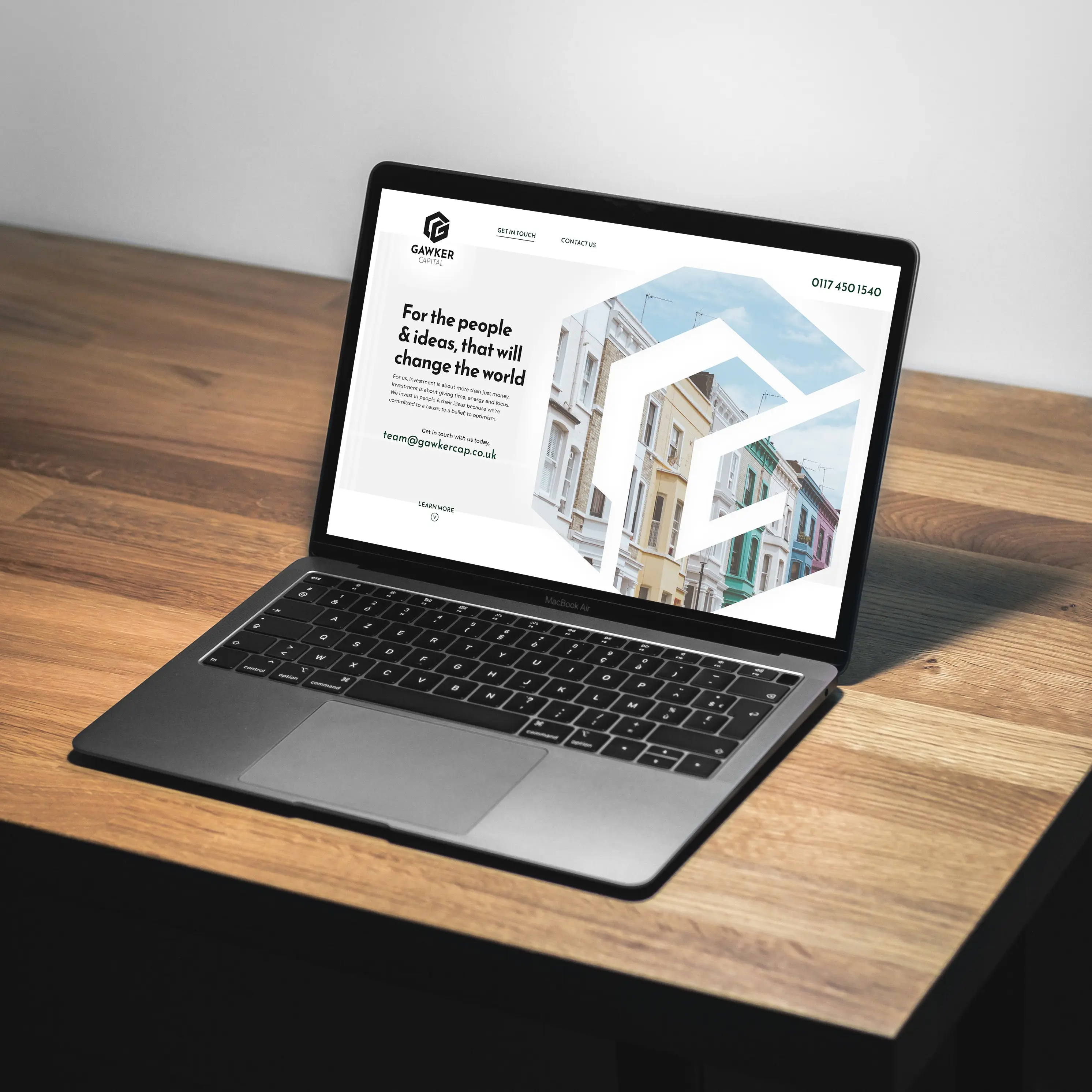 A mockup of a website design for a venture capital company. A Macbook computer sitting on a wooden table, showing off the landing page of a beautiful light themed website.