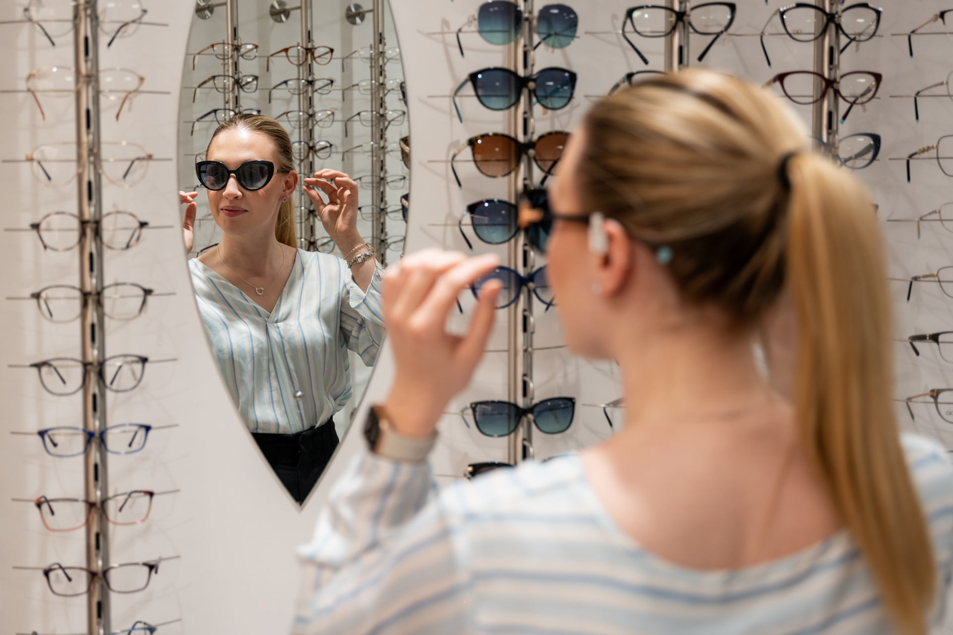 Woman trying on sunglasses in optical store with many frames displayed