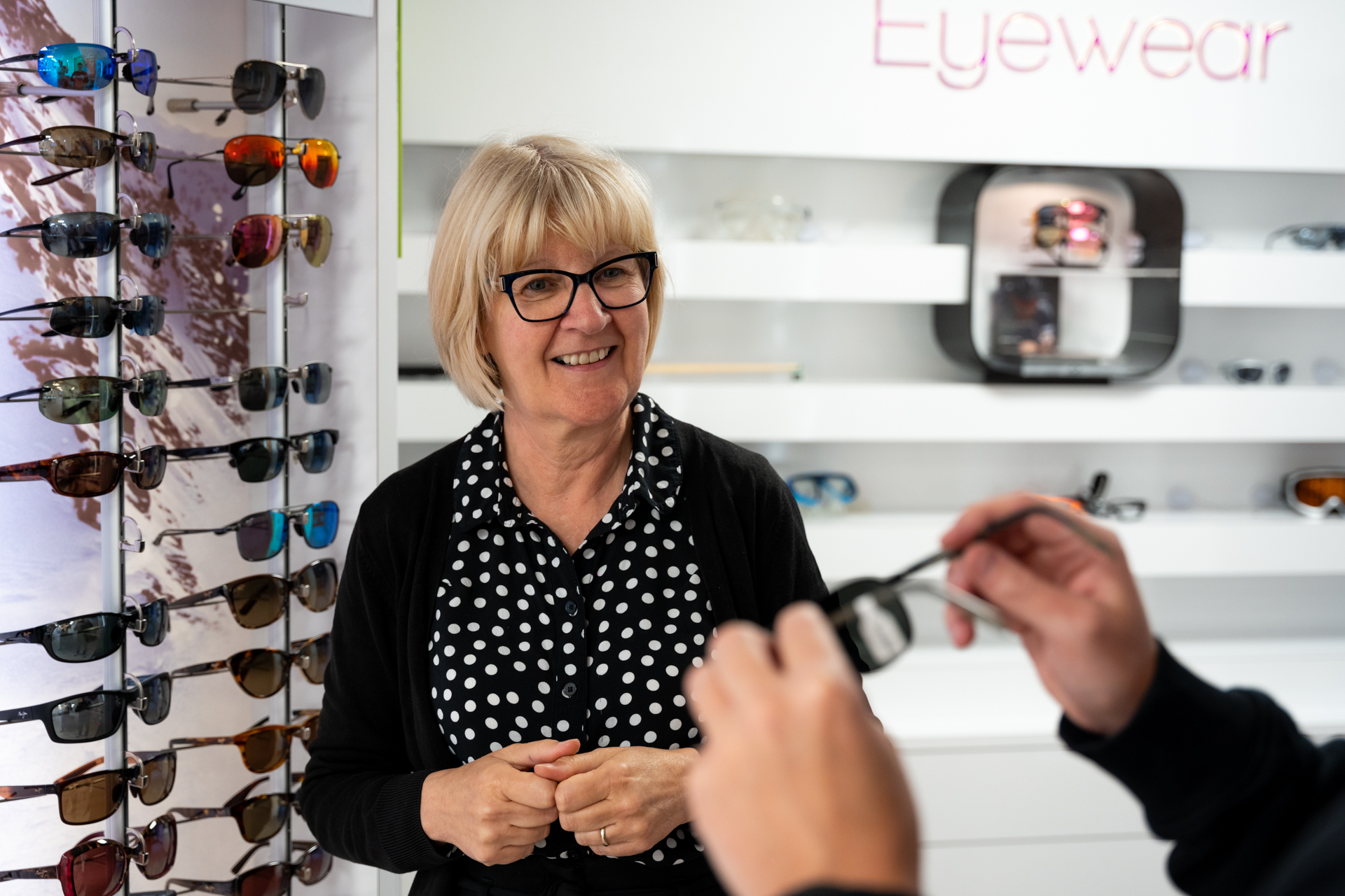 Smiling optician standing in eyewear store with sunglasses display