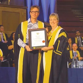Two people in academic robes holding an award certificate on stage
