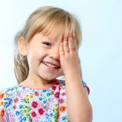 Smiling child covering one eye with hand, wearing colorful floral top