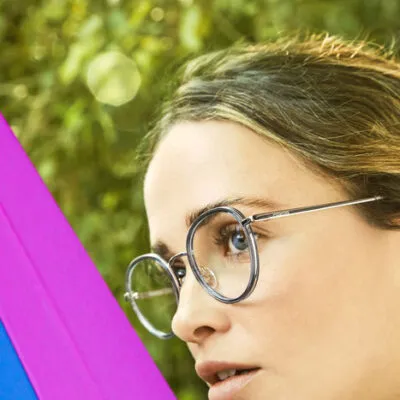 Person with glasses looking sideways against blurry green background