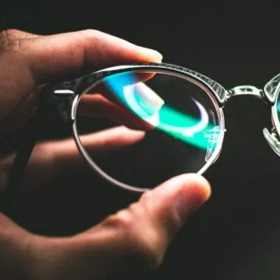 Hand holding round glasses with colorful light reflection on lens